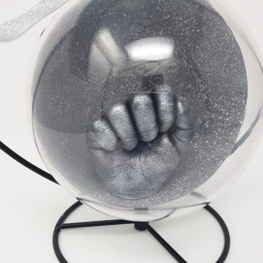 Close-up of a silver hand cast in a clear bauble with heart stand