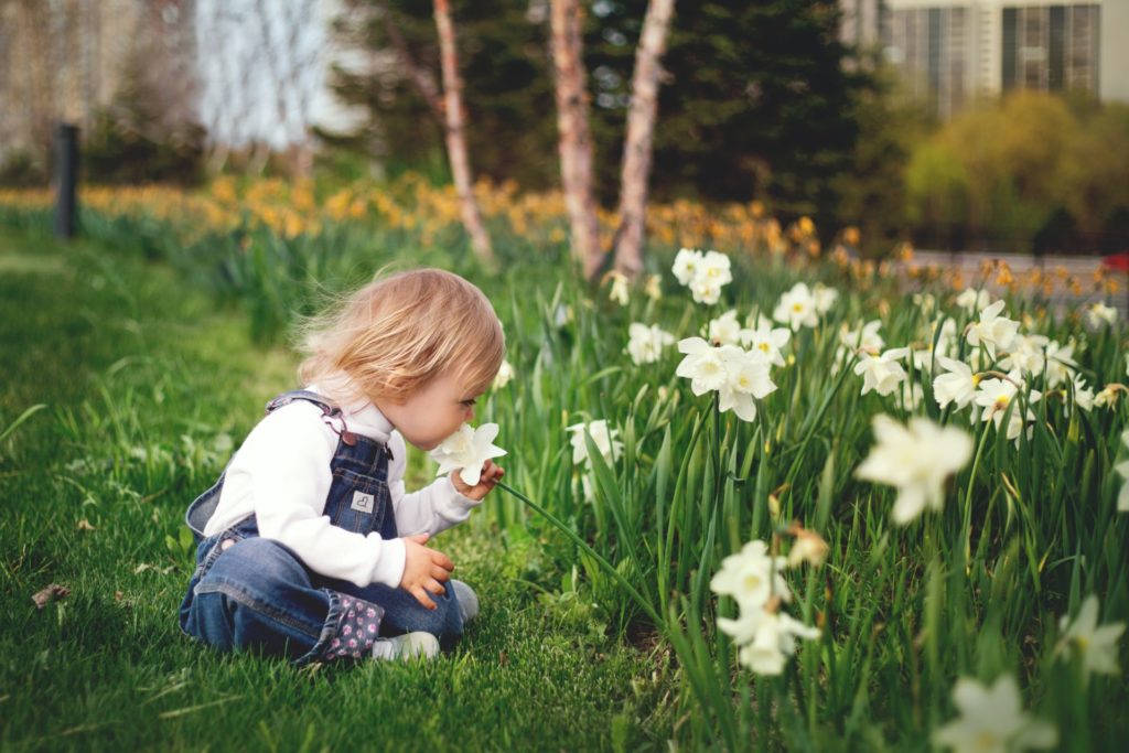 Girl sitting on grass smelling white flower